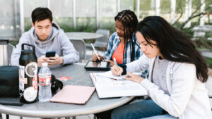 Three diverse students studying at a table outside