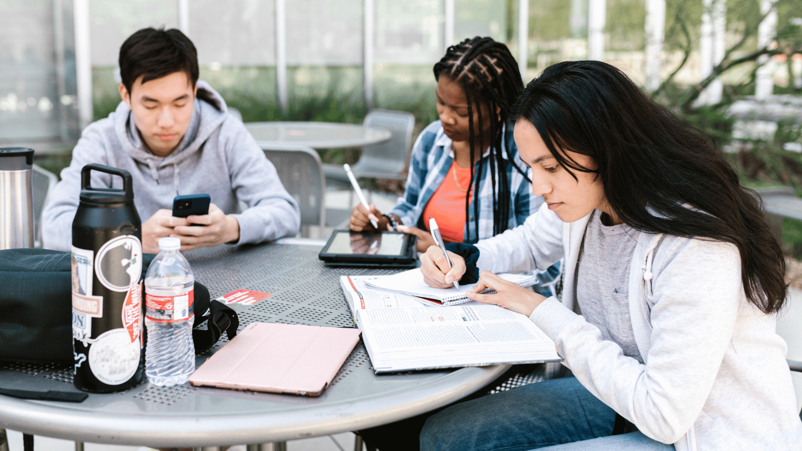 Three diverse students studying at a table outside