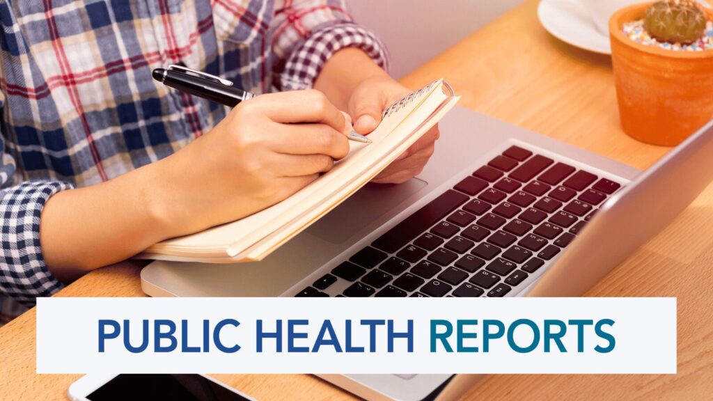 A male student taking notes with a pen and pad near a laptop