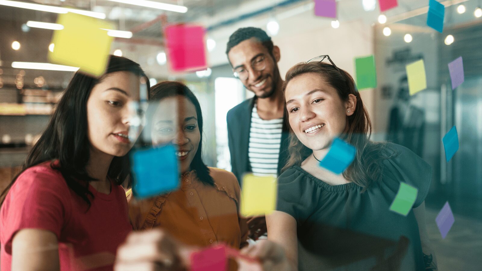 Group of coworkers looking at post-its on a glass wall
