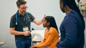 A pediatrician examing a young girl during a consultation as her parent watches