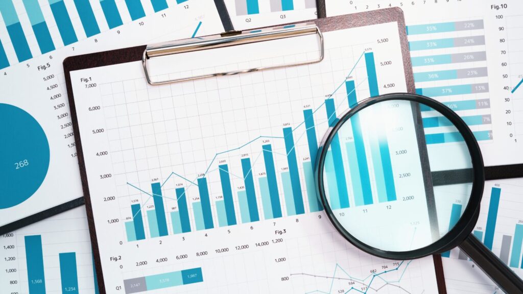 A magnifying glass placed over financial charts and graphs on a clipboard, emphasizing data analysis and business performance trends