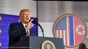 Former President Donald Trump speaking at a podium with the flag of the United States in the background