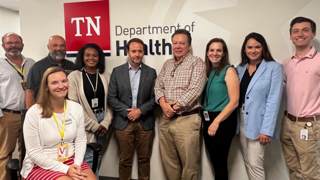 A group of nine people stands in front of a sign that reads TN Department of Health. They are smiling and posed for a group photo_1600x900