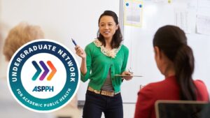 A woman in a green cardigan speaks to a group in a classroom. The Undergraduate Network for Academic Public Health logo is visible on the left