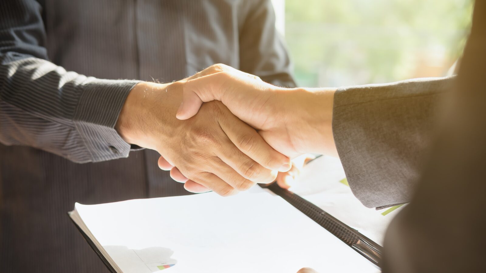 Close-up of a handshake between two individuals, symbolizing partnership or agreement, with a document in the foreground and soft lighting in the background