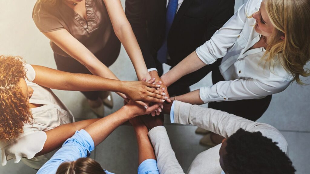stock image of a group of people standing in a circle  with their hands gathered in the middle 