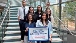 Group photo of eight ASPPHCDC Public Health Fellowship Program fellows, Class of 2024, standing on a staircase. Two fellows hold a program sign