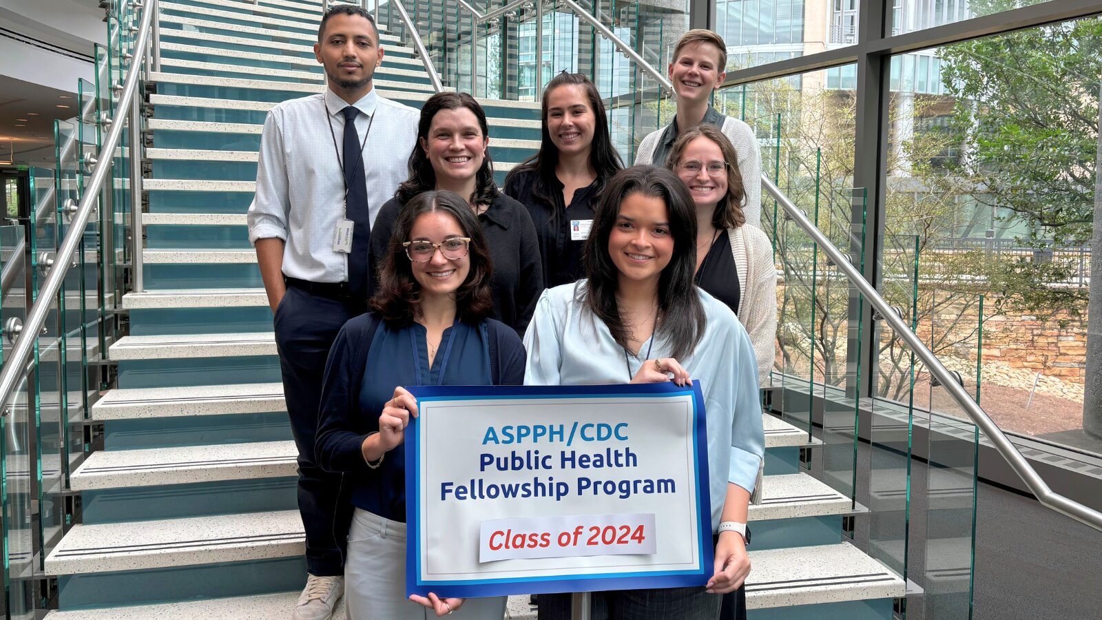 Group photo of eight ASPPHCDC Public Health Fellowship Program fellows, Class of 2024, standing on a staircase. Two fellows hold a program sign