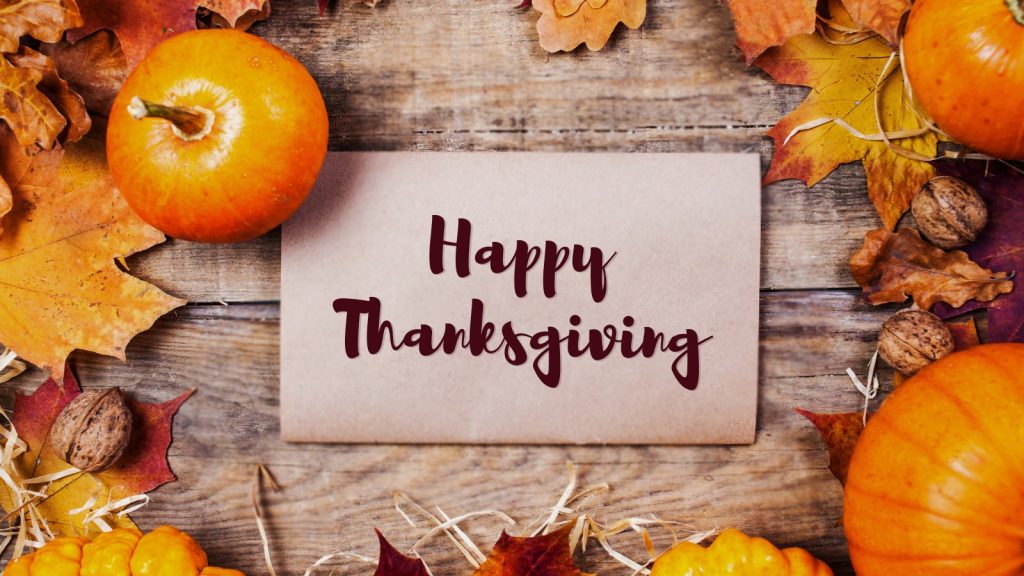 Festive Thanksgiving greeting card with pumpkins, colorful autumn leaves, walnuts, and 'Happy Thanksgiving' text on rustic wood