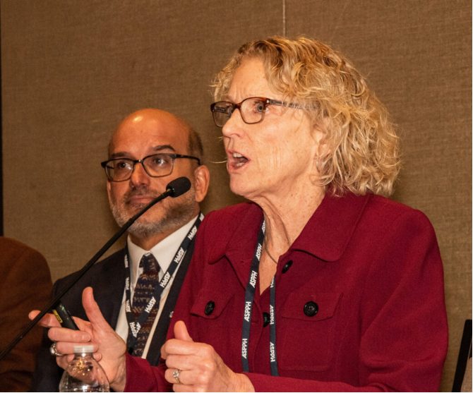 A female-presenting person speaking into a microphone at a conference