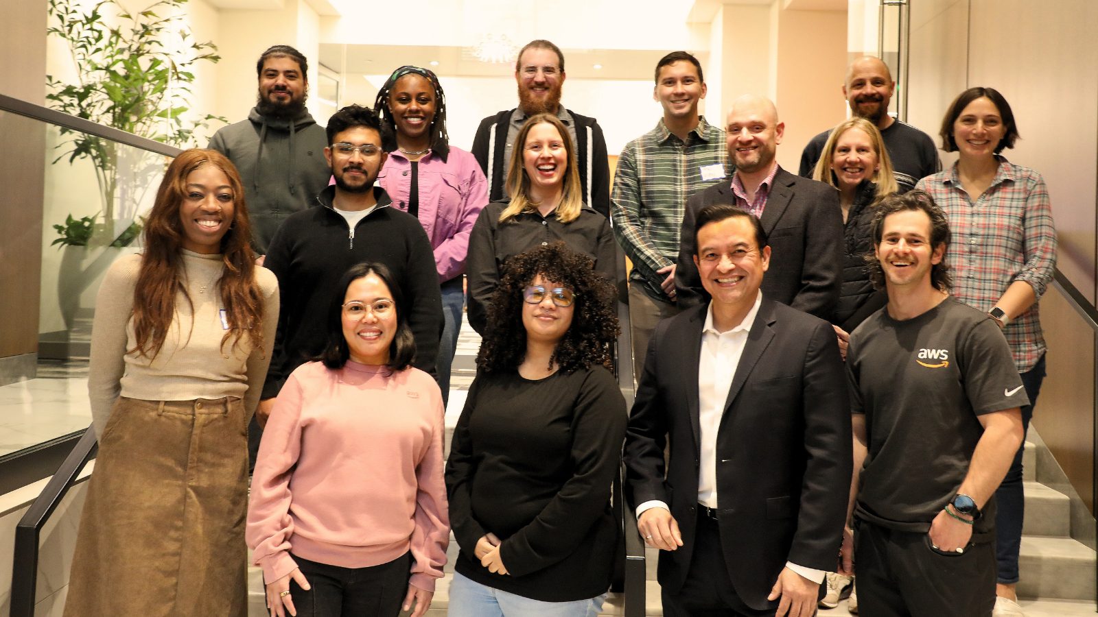 Group photo of ASPPH and AWS staff smiling on a staircase during Amazon Q Developer Immersion Day in a modern indoor setting