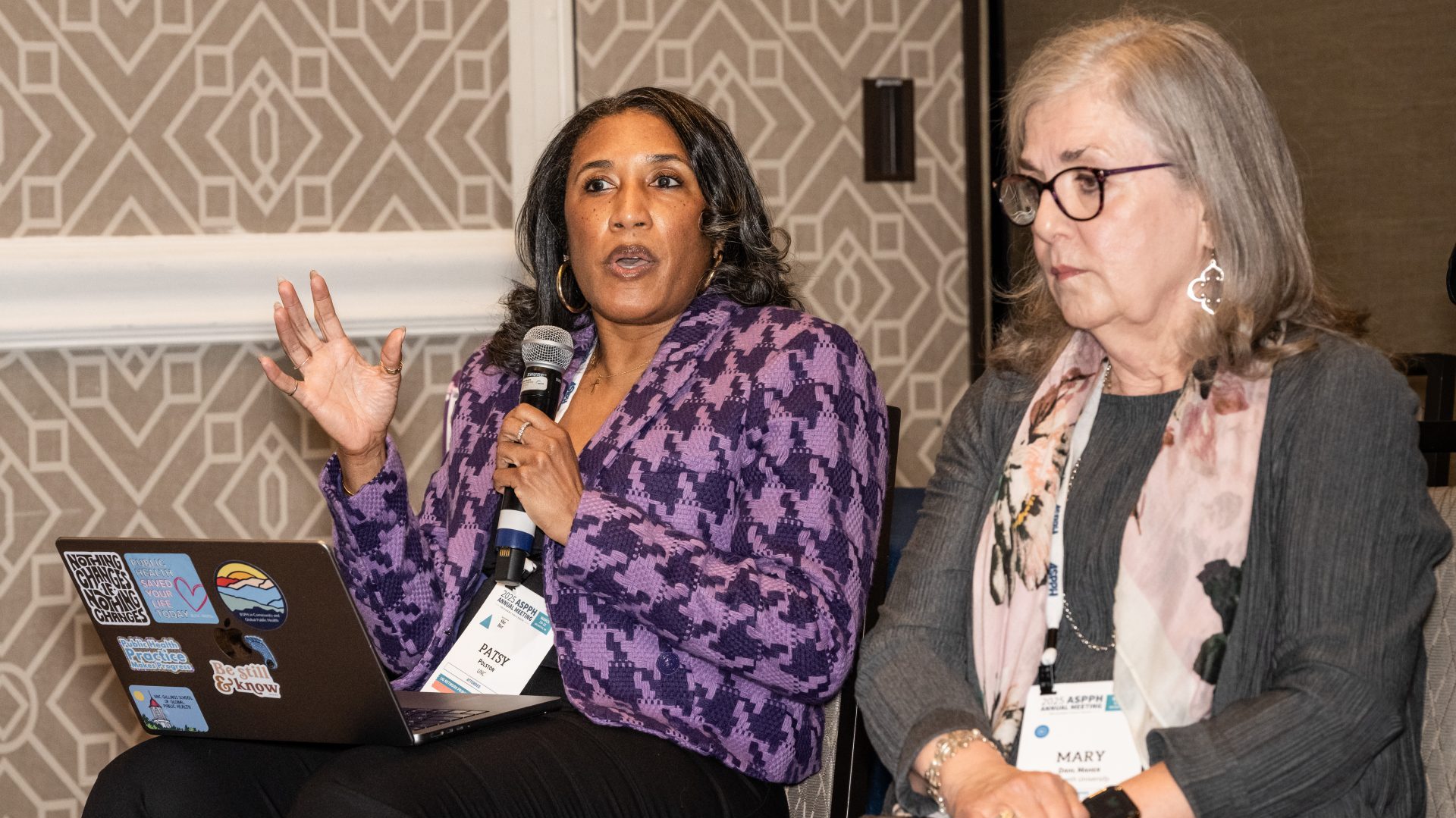 Two women sitting as one speaks into a microphone