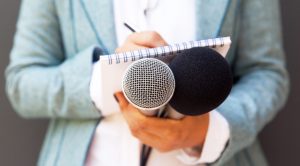 Person holding two microphones and a notepad