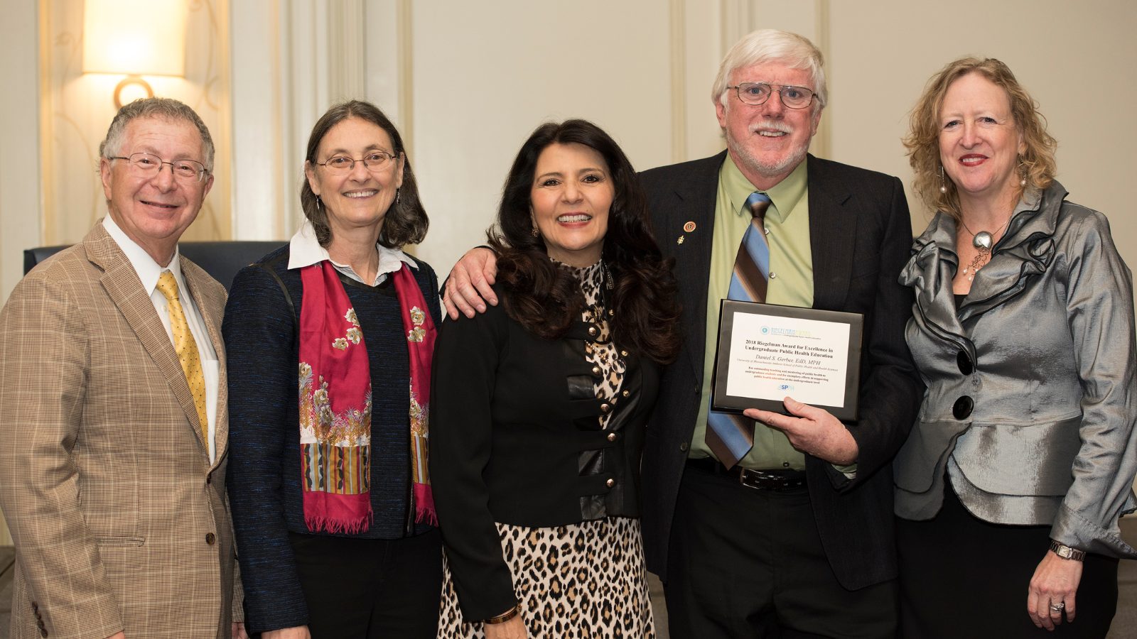 Dan Gerber, smiling and holding an award plaque, stands with four colleagues at an indoor recognition ceremony