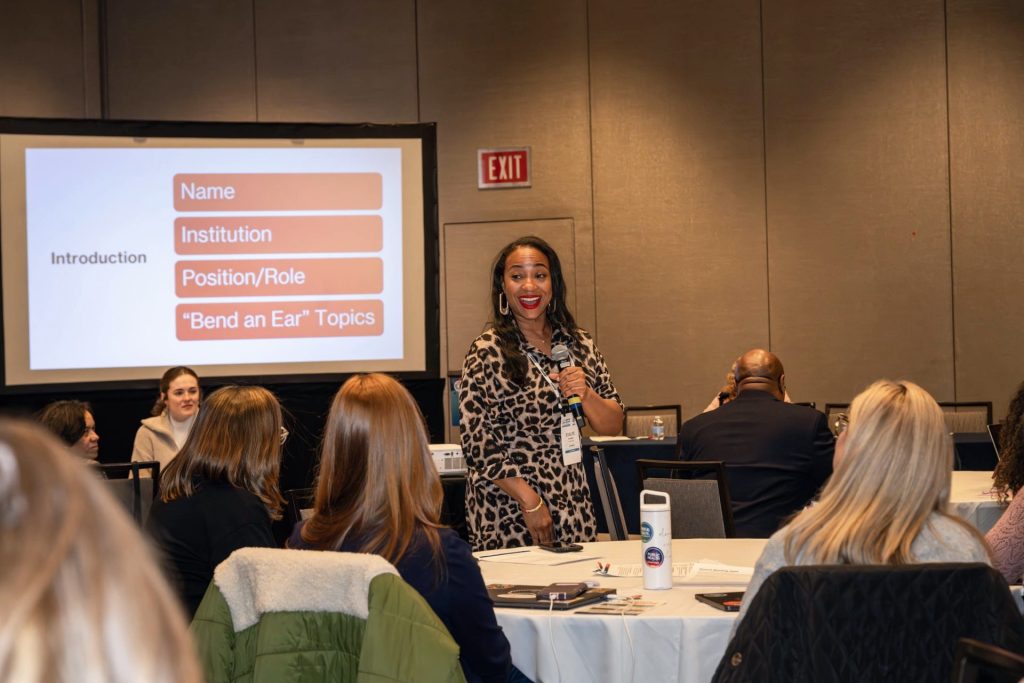 Woman speaks into a microphone in front of a room full of people