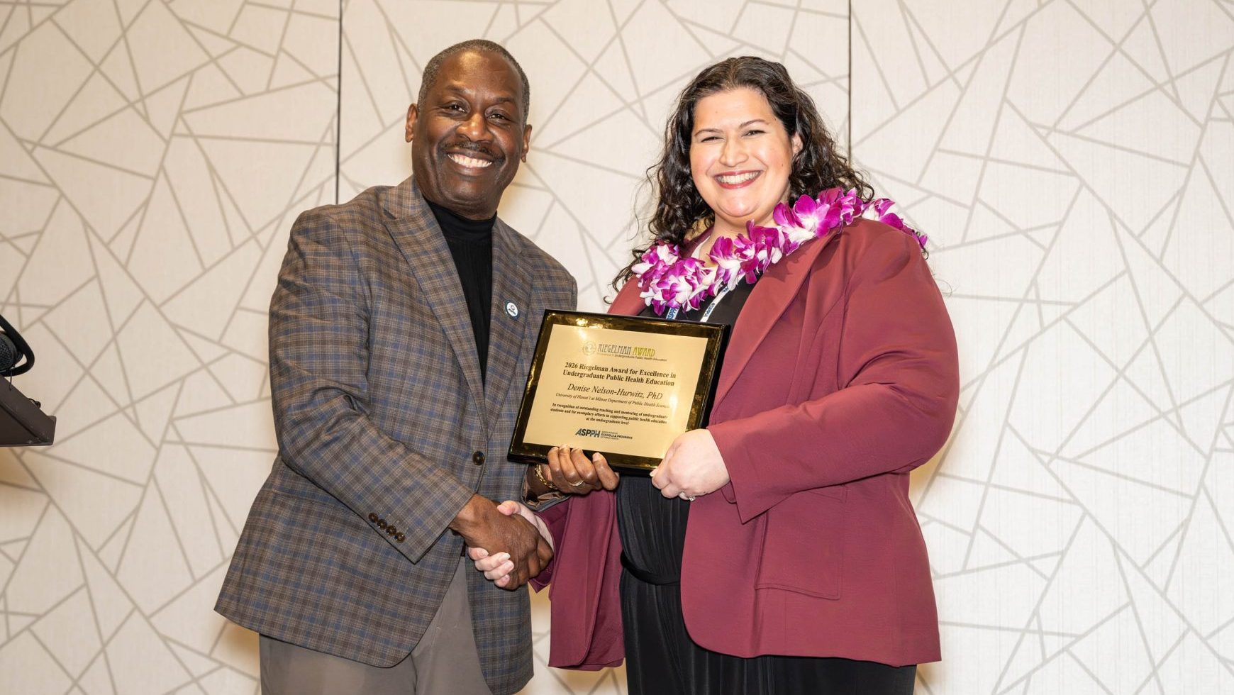 A man and woman stand on stage holding an award plaque