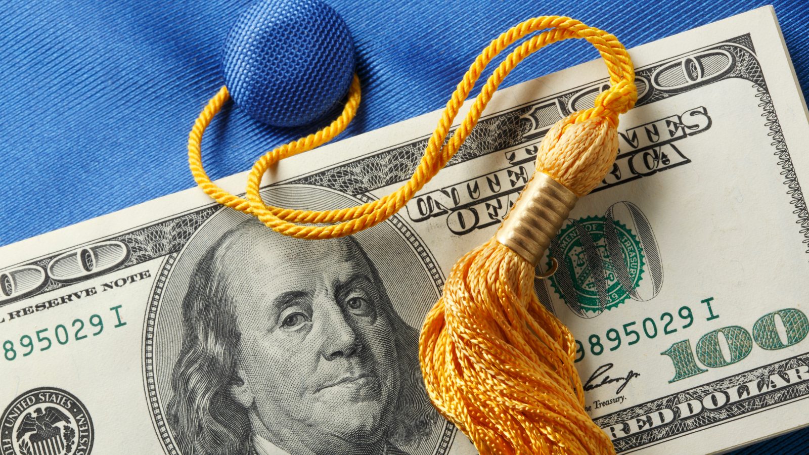Close up image of one hundred dollar bill on top of graduation cap