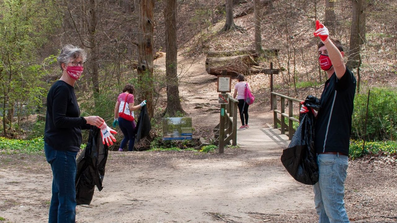 Four people carrying trash bags picking up litter in nature.