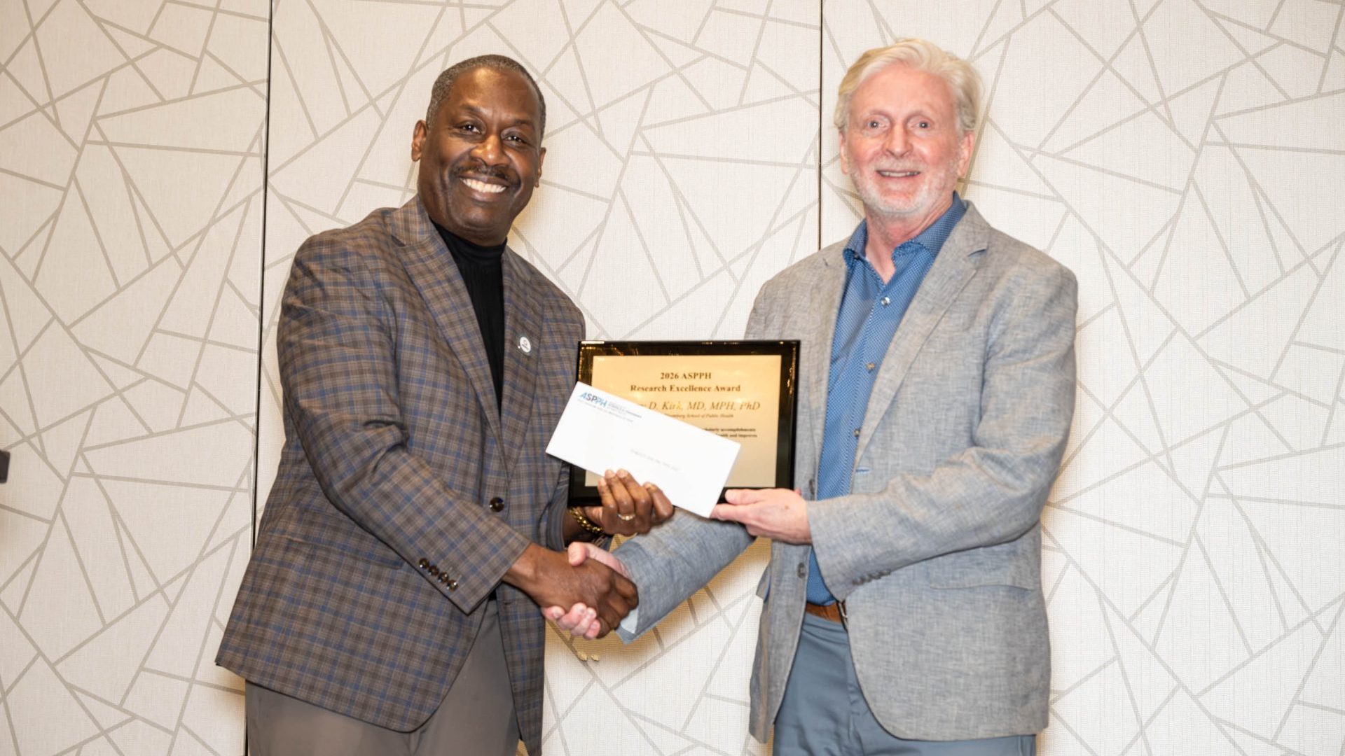 A man holding an award stands next to another man
