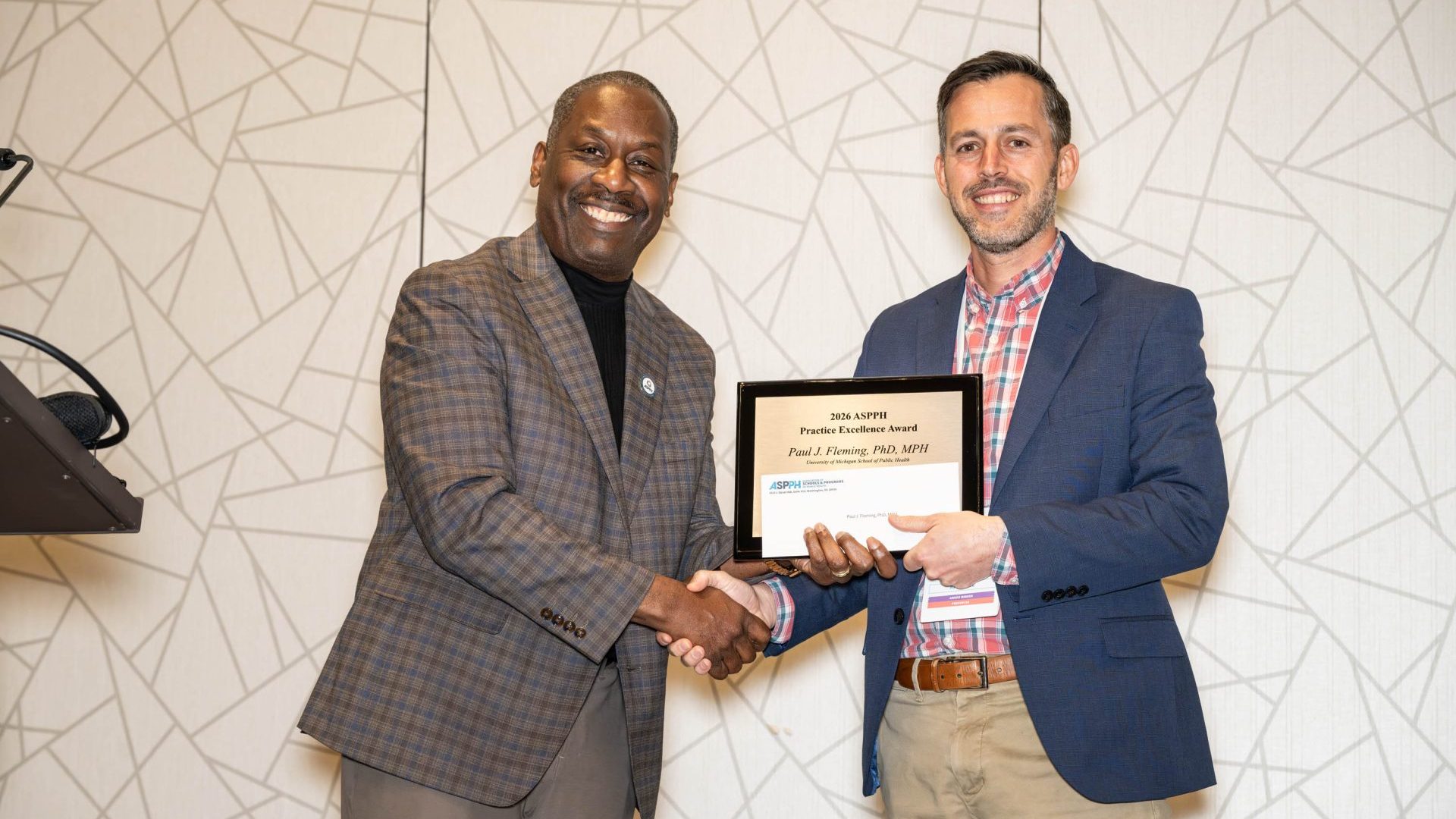 A man holding an award shakes hands with another man
