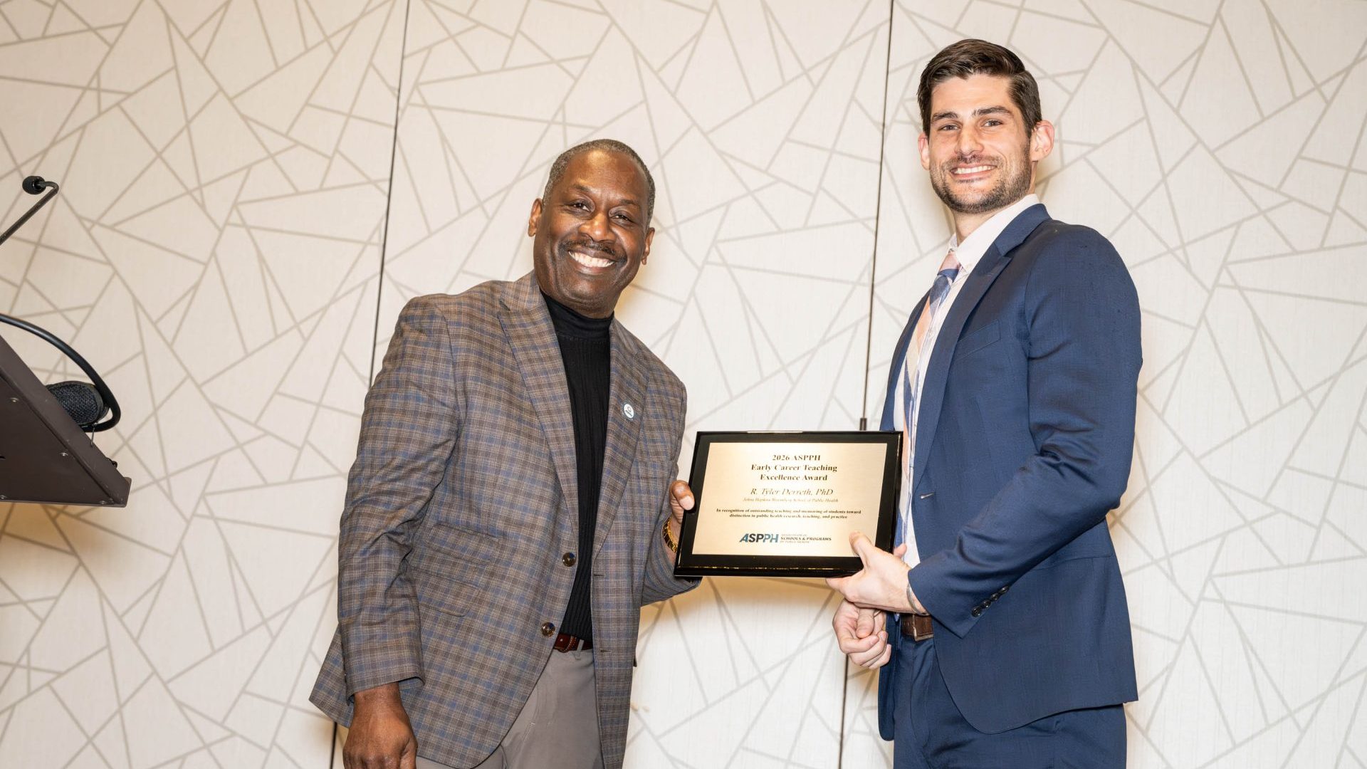 Two men stand on stage holding an award