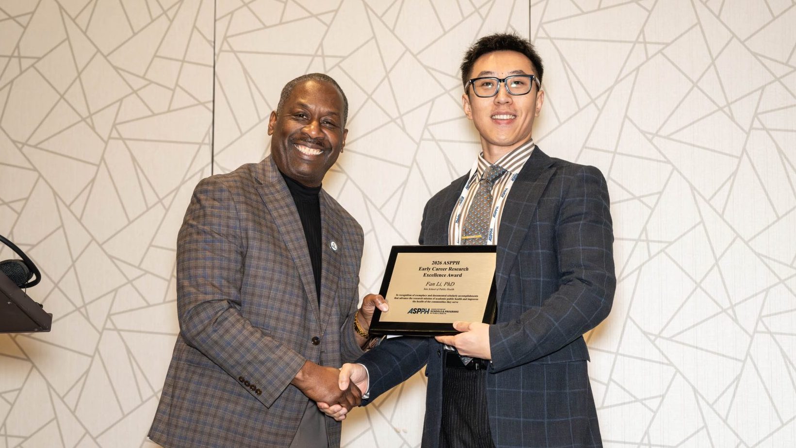 Two men shake hands while holding an award