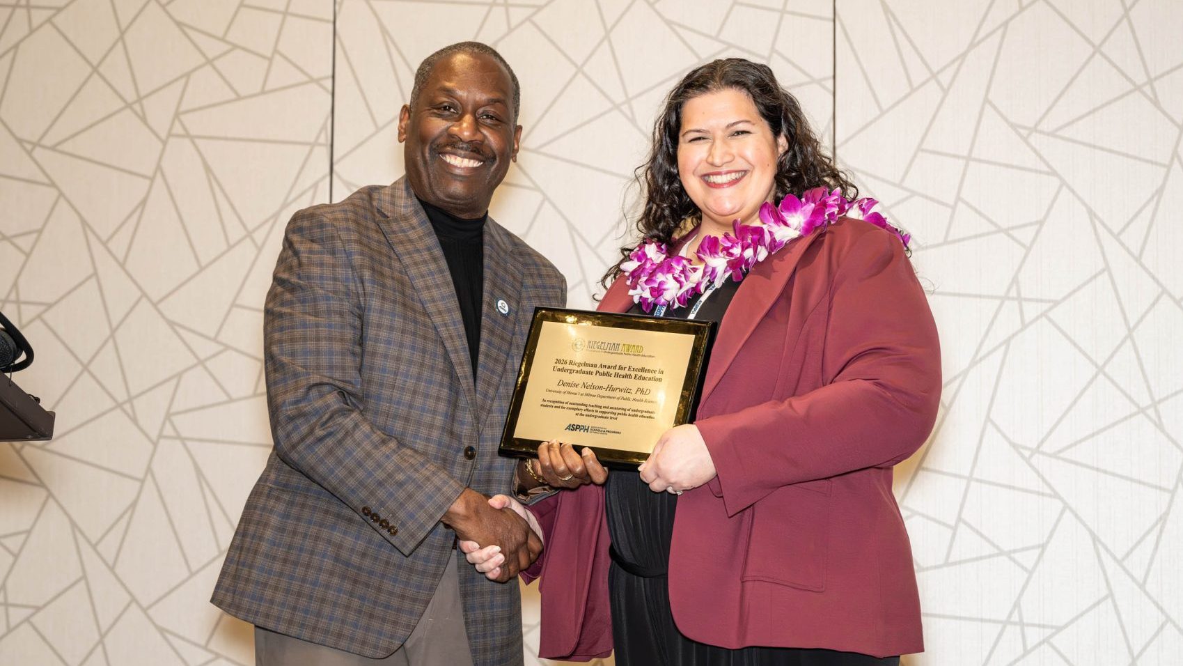 A man and woman shake hands while holding an award
