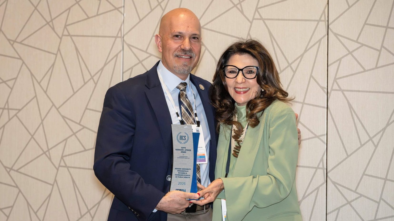 A man holding an award stands next to a woman in a green suit