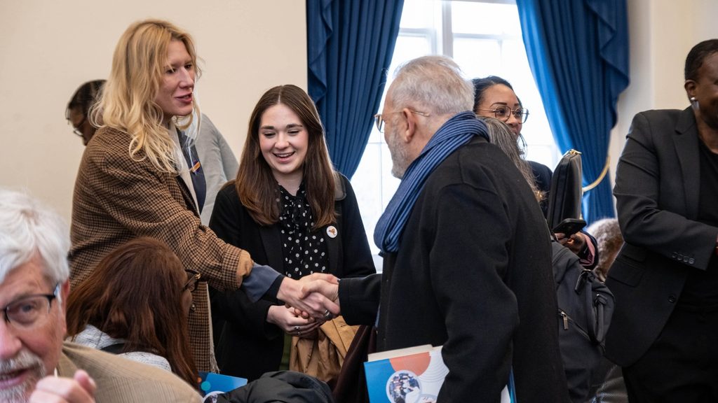 Two members shake hands in front of group of people