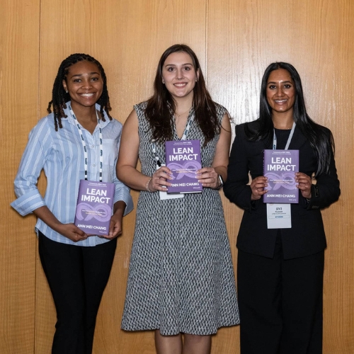 Three students holding purple books titled "Lean Impact"